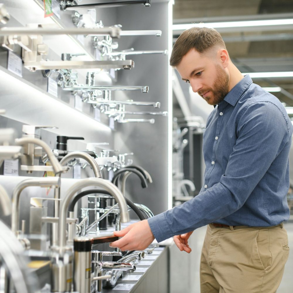 A large selection of water faucets. Man chooses a products in a sanitary ware store